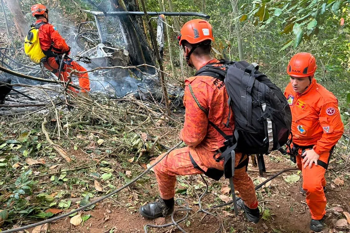 Firefighters in orange gear near a burning structure outdoors.