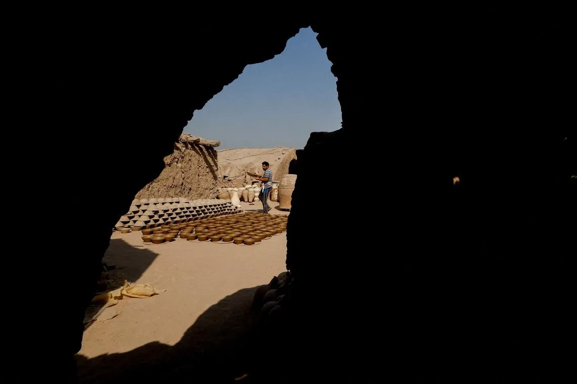 An Iraqi worker carrying a clay pot at a workshop in the holy city of Najaf, Iraq, Sep 9, 2024. 