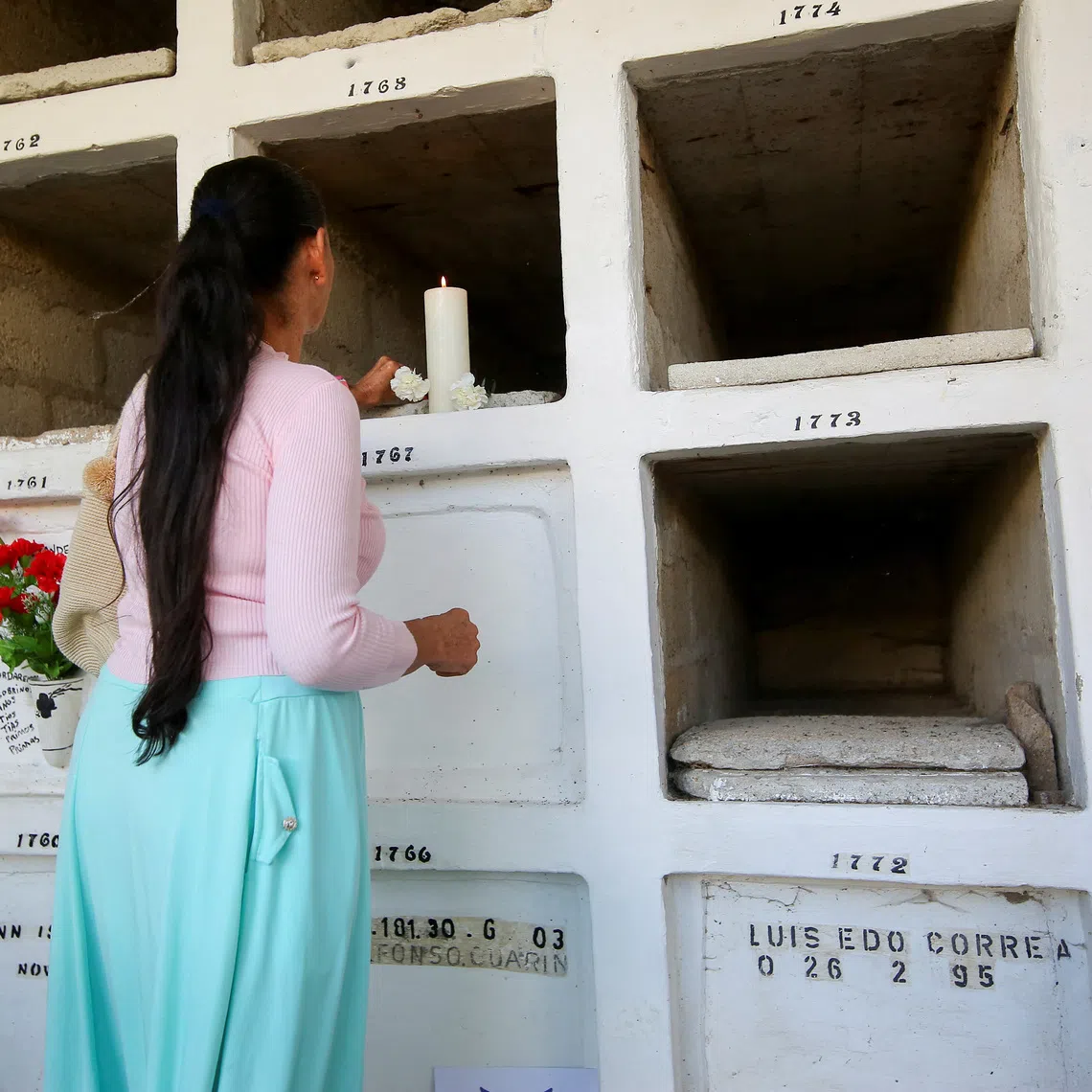 Roselly Gil lights a candle at a cemetery during the exhumation of remains believed to be those of her brother Jesus Arbey, who disappeared in 2003, in Rionegro, Colombia, March 10, 2024. REUTERS/Juan David Duque