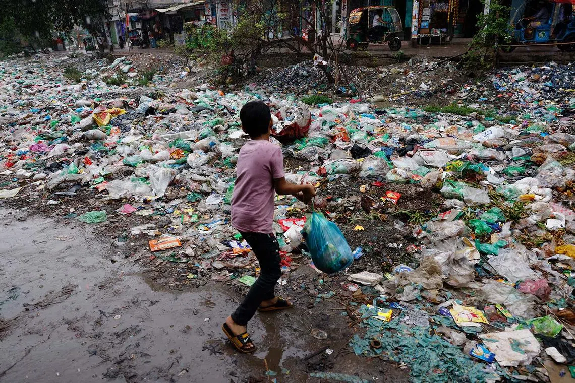 A boy throwing a polythene bag full of waste into Shuvadda Canal which is under the pile of plastic waste, in Dhaka, Bangladesh, May 20, 2025. 