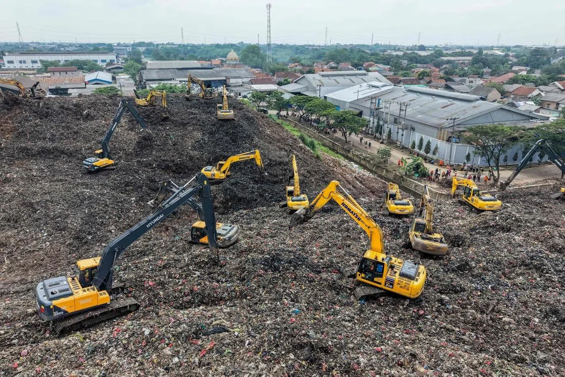 This aerial picture shows a rescue team using heavy machinery to search for people following a landslide at Bantargebang landfill in Bekasi, West Java, on March 9, 2026. A landslide on Indonesia's biggest landfill buried trucks and food stalls, killing four people, rescuers said on March 9 as they searched for at least five more reported missing. (Photo by BAY ISMOYO / AFP)