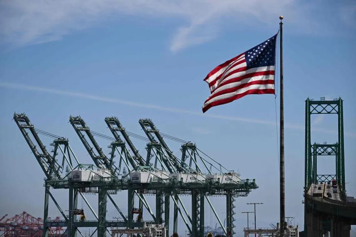 The US flag blows in the wind as trucks drive on the Vincent Thomas Bridge past cranes to unload cargo shipping containers at the Port of Los Angeles in San Pedro, California on April 10, 2025. US President Donald Trump's 10 percent tariff for almost all countries except China will likely remain in place going forward, his top economic advisor Kevin Hassett said Thursday. On April 8, Trump announced a 90-day pause on higher tariffs against all countries except China, reversing a policy that had roiled global stock markets and spooked the American bond markets -- a key barometer of investors' faith in the US government's ability to pay its debts. (Photo by Patrick T. Fallon / AFP)