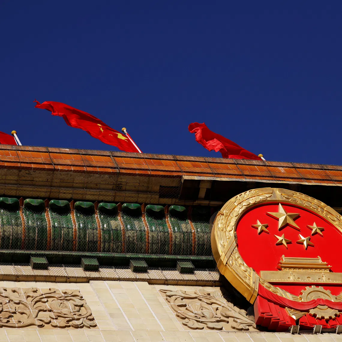 A Chinese flag flutters above the national emblem on the Great Hall of the People before the opening session of the National People's Congress (NPC) in Beijing, China March 5, 2022. REUTERS/Carlos Garcia Rawlins
