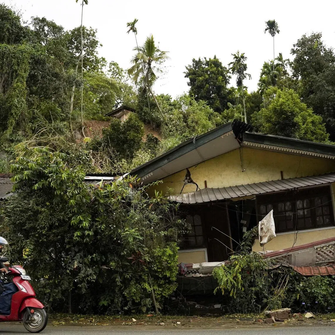 A man rides a scooter past a damaged house following Cyclone Ditwah, at Kandekumbura in Kandy District, Sri Lanka, on Dec 5. 