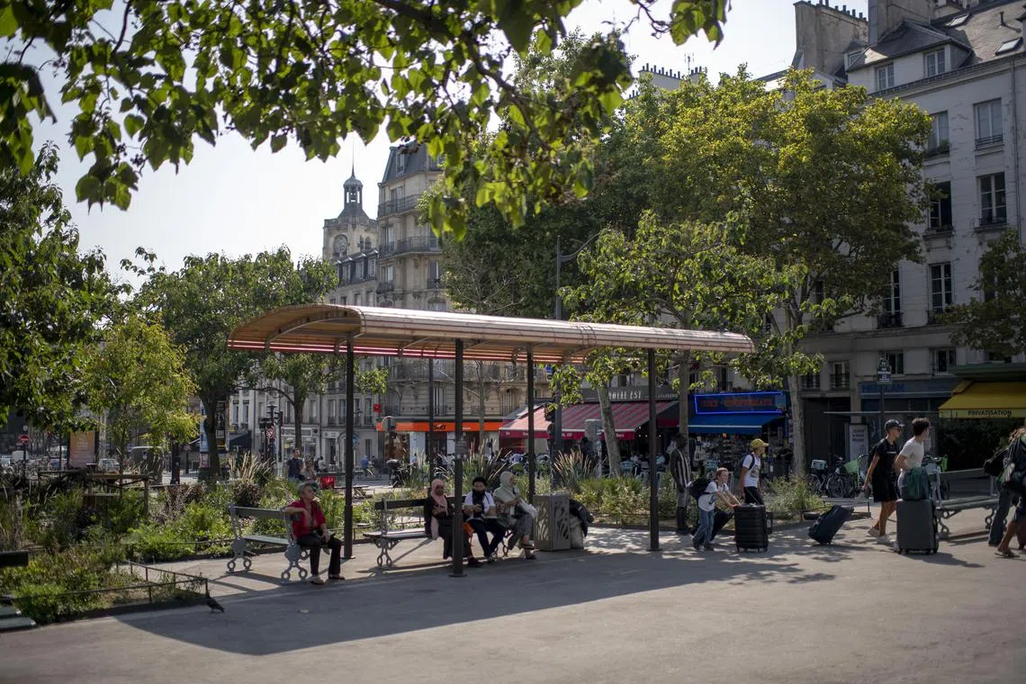 Taking cover near a train station in Paris, Aug. 14, 2025. Where the city cannot plant trees, officials are putting up more shade structures and water misters to offer solace during hot days. (Dmitry Kostyukov/The New York Times)