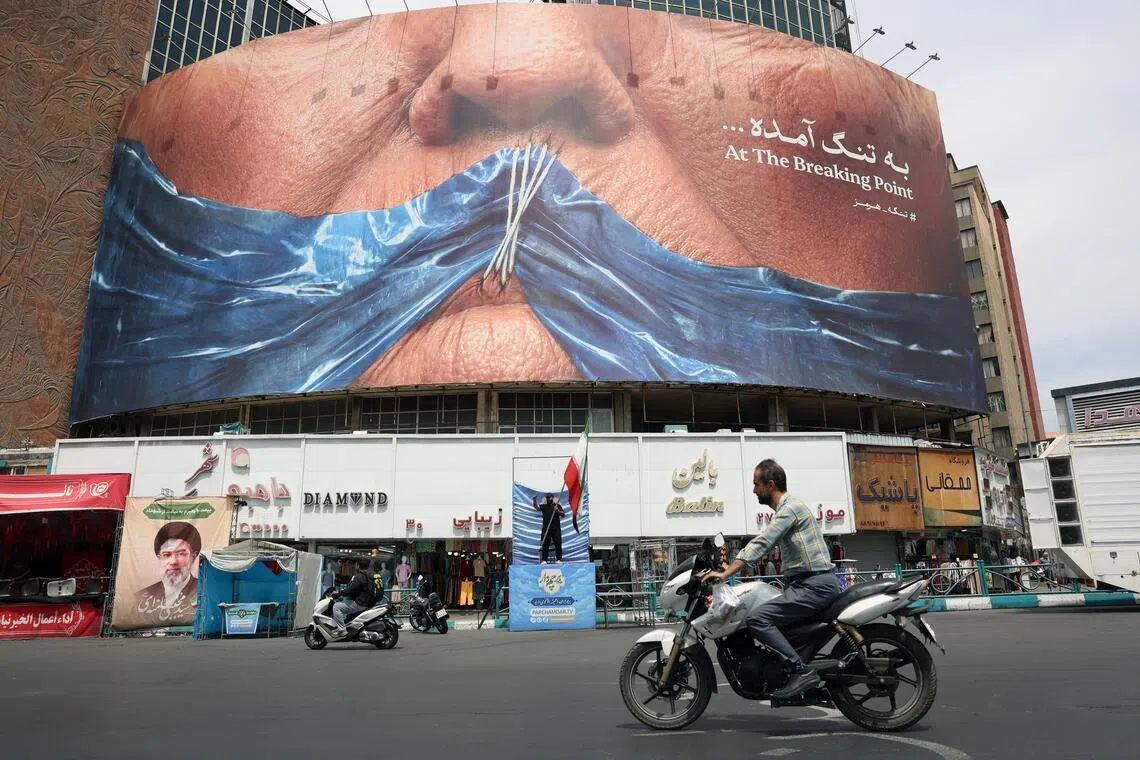 Iranians drive in front of a large anti-US billboard featuring US President Donald Trump and the Strait of Hormuz in Tehran.
