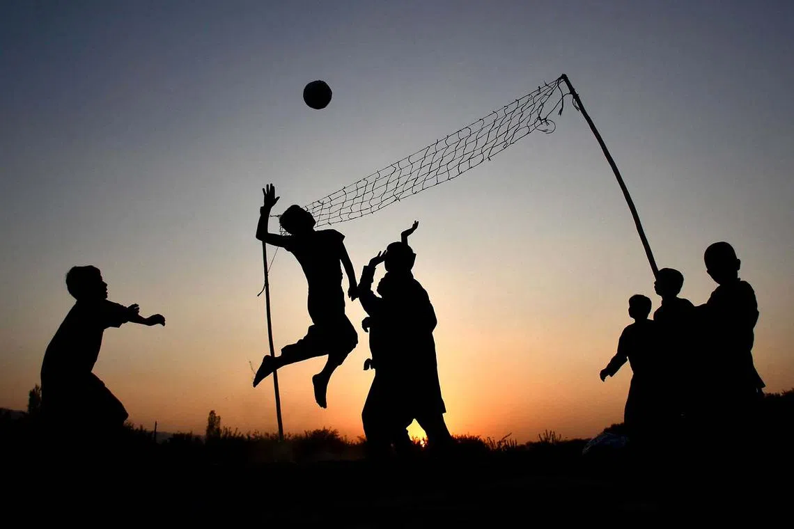 TOPSHOT - Afghan youths play volleyball at a field during sunset in Chimtal district of Balkh province on October 16, 2024. (Photo by Atif ARYAN / AFP)