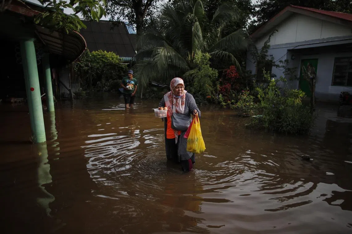 A woman holds food while walking through flood waters in Klang,  Selangor on Nov 12. A total of 719 victims in and around the Klang district were moved to seven relief centres.
