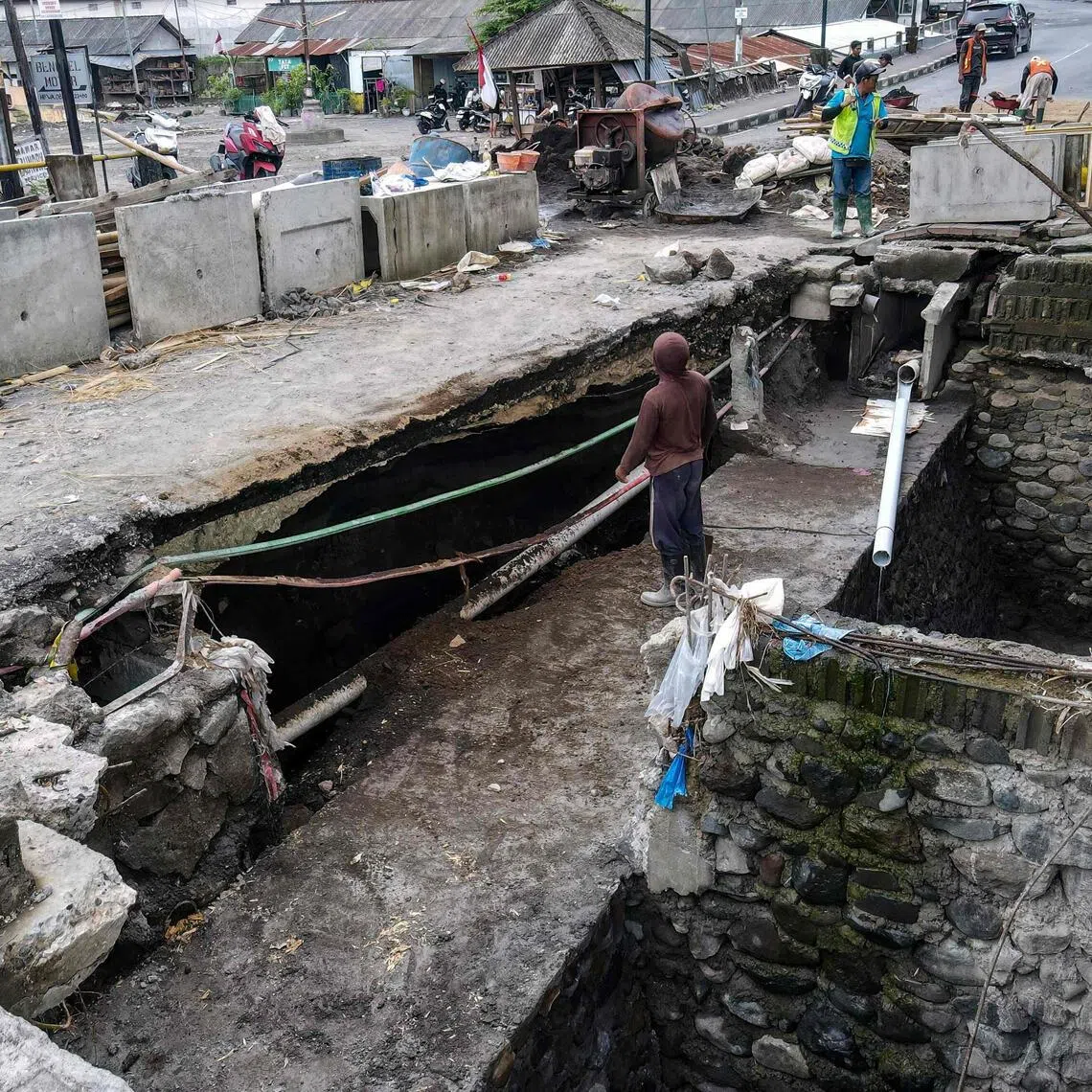 This picture taken on October 1, 2025 shows workers repairing an area where a large sinkhole formed during recent flooding in Badung, on Indonesia's resort island of Bali. Devastating flash floods that killed at least 18 people and left four missing was the island's worst in a decade, according to Indonesia's Meteorology, Climatology and Geophysics Agency (BMKG). It was caused partly by record rain, but was also a reckoning for years of rampant overdevelopment and a waste management system under enormous strain. (Photo by BAY ISMOYO / AFP) / To go with AFP STORY Indonesia-Bali-flood-climate-waste, Focus by Marchio GORBIANO