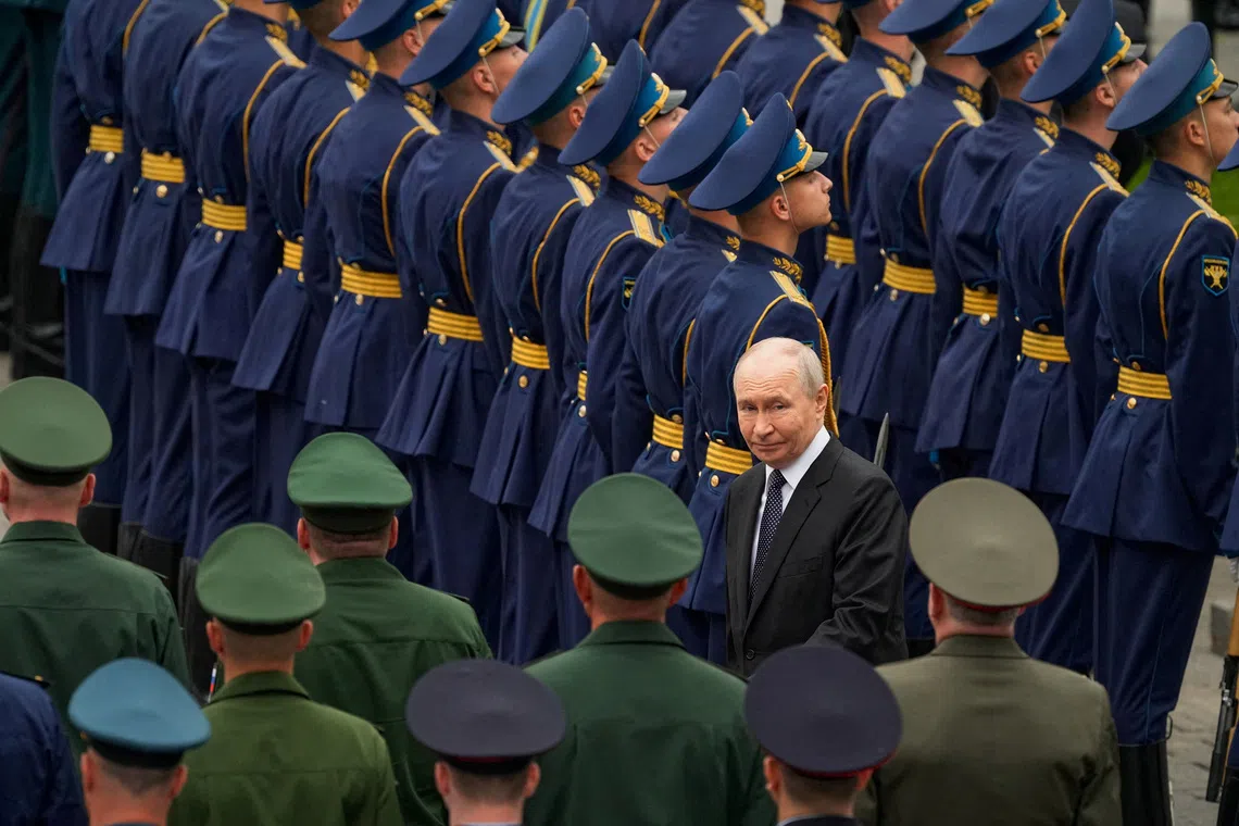 A man in a suit stands before a group of people in uniforms and civilian clothes.