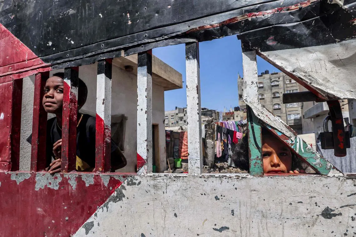 Children look on from behind a gate  painted in the colours of the Palestinian flag, in Rafah in the southern Gaza Strip.