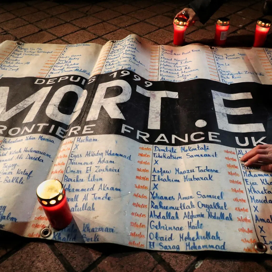 People place candles around a list of names of migrants that have died since 1999 while trying to cross the English Channel, during a tribute to the 27 migrants who died when their dinghy deflated as they attempted to cross the English Channel, at the Richelieu Park in Calais, France, November 25, 2021. REUTERS/Pascal Rossignol
