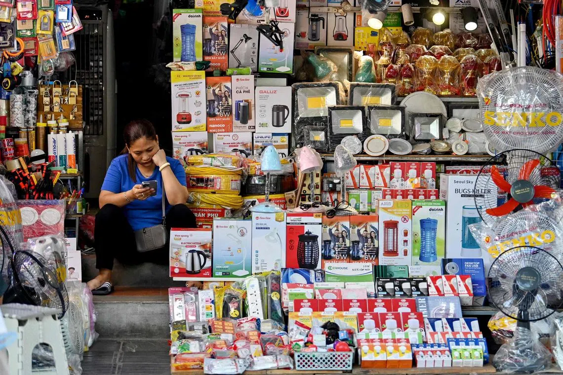 A seller of household electrical appliances uses a mobile phone as she waits for customers at a shop in Hanoi on June 28, 2024. (Photo by Nhac NGUYEN / AFP)