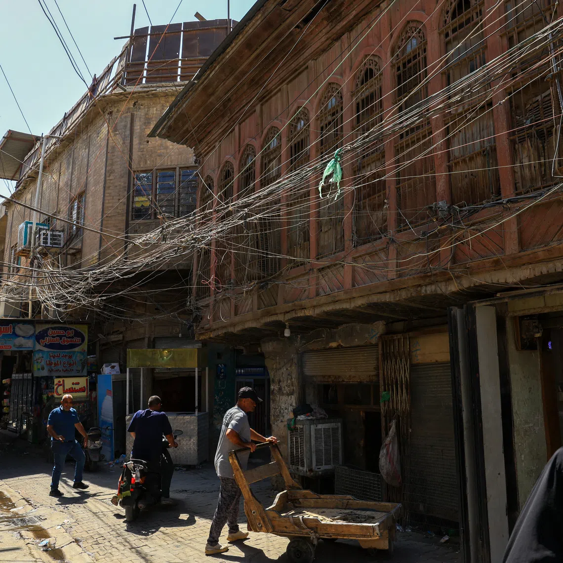 People walk along an old street as a tangled web of electrical wires from a generator supplying homes with electricity hangs above buildings, in Baghdad, Iraq, September 10, 2025. REUTERS/Thaier Al-Sudani