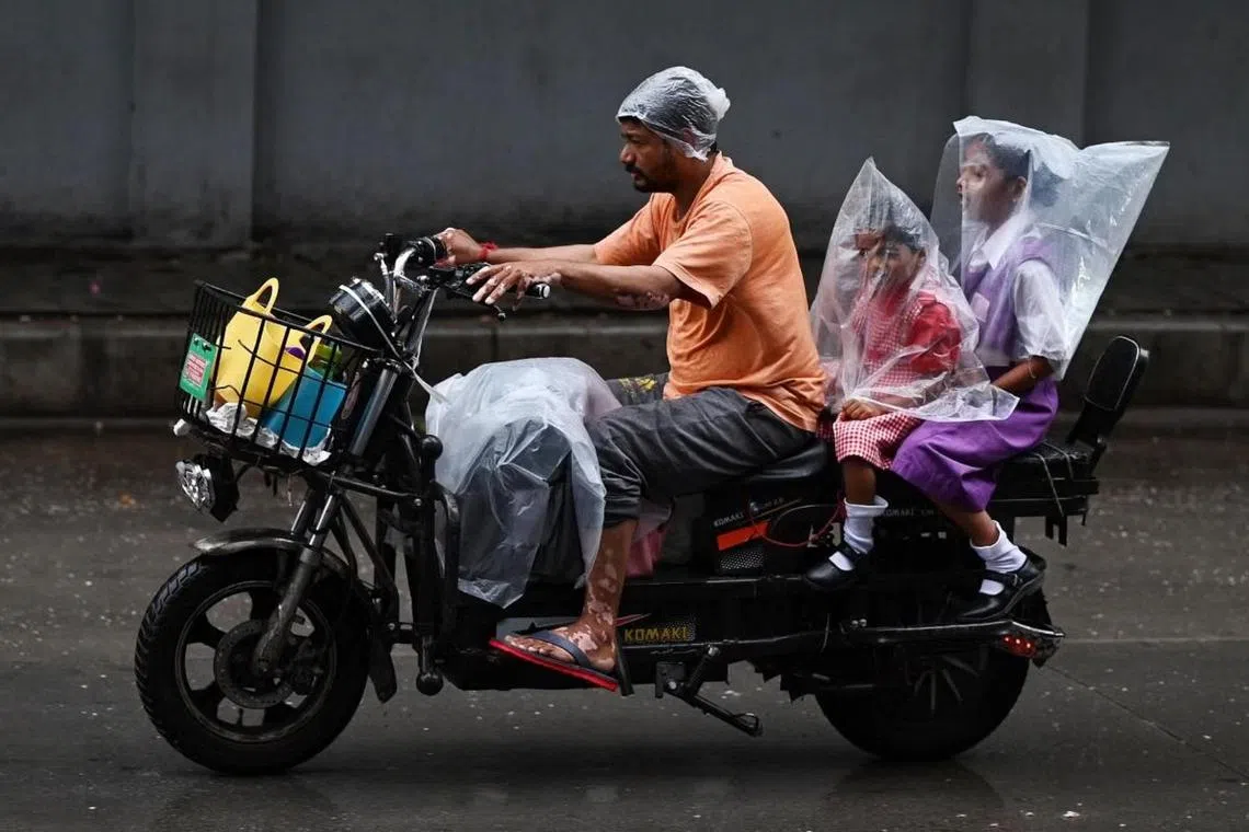 A man riding a two-wheeler with two children covered with plastic sheets during a monsoon downpour in Hyderabad on July 18, 2023.