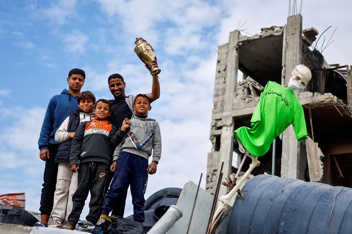 Palestinian soccer player Ahmed Al-Loulahi holds a trophy he retrieved from his destroyed house as he poses with his children on the rubble, with his jersey hanging, amid a ceasefire between Israel and Hamas, in Rafah in the southern Gaza Strip, January 22, 2025. REUTERS/Mohammed Salem TPX IMAGES OF THE DAY