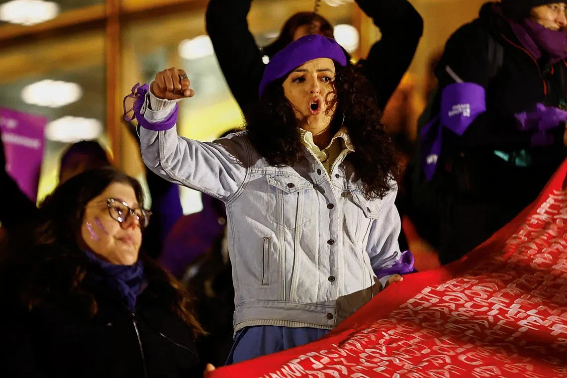 A woman gestures while holding a banner, featuring the names and ages of female victims of male violence, in Paris, France. 