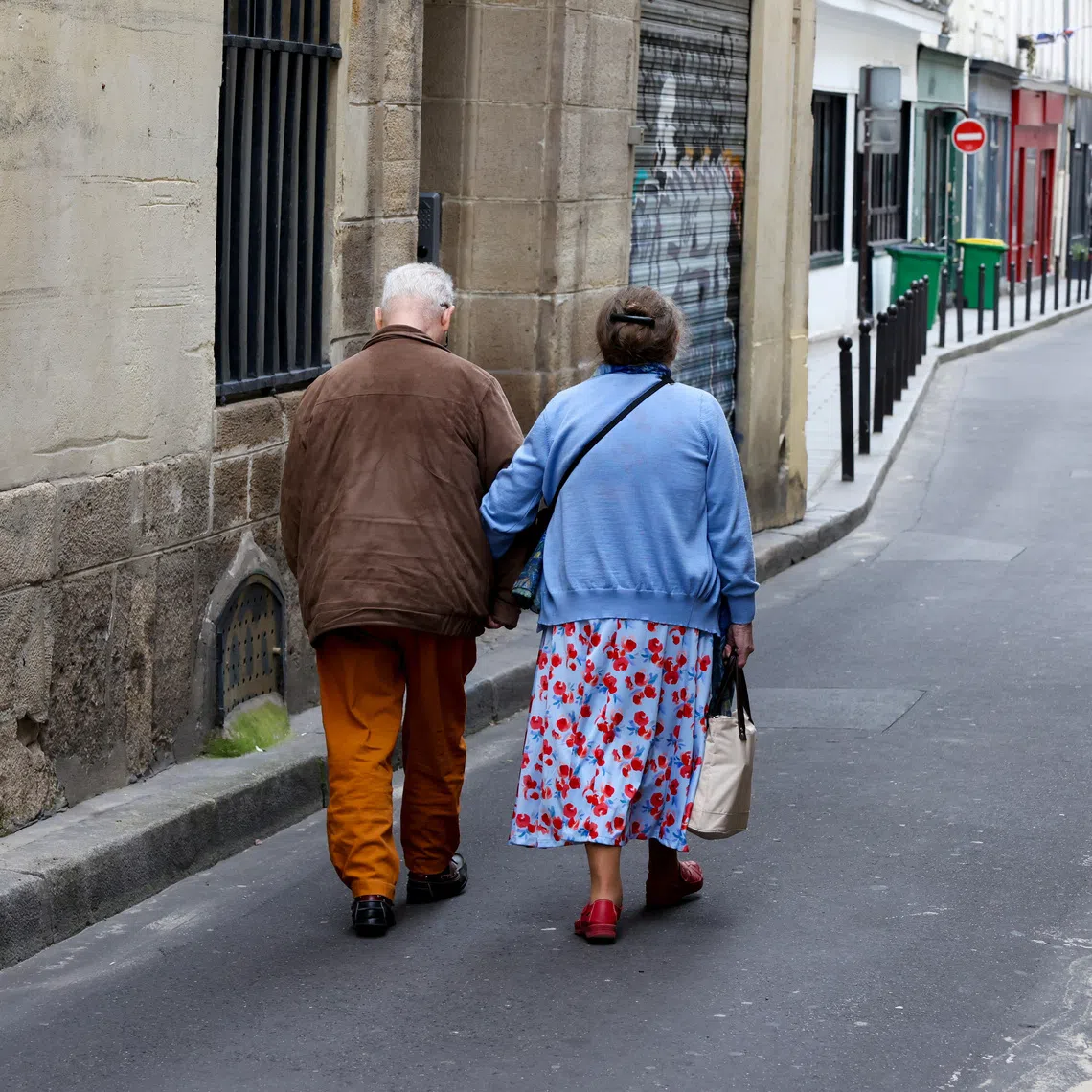Two elderly people walk arm-in-arm down a side street in Paris, France, July 14, 2024. REUTERS/Kevin Coombs