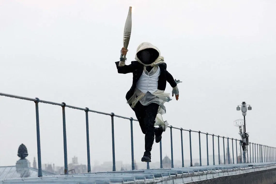 TOPSHOT - Paris 2024 Olympics - Opening Ceremony - Paris, France - July 26, 2024. A torchbearer runs atop the Musee d'Orsay during the opening ceremony. (Photo by Peter Cziborra / POOL / AFP)