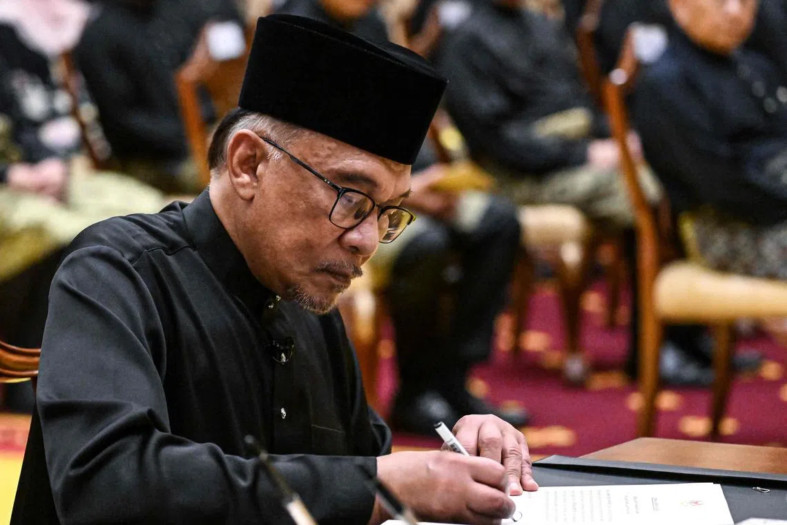 Malaysia's new Prime Minister Anwar Ibrahim signs documents after taking the oath during the swearing-in ceremony, on Nov 24, 2022.