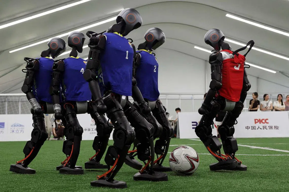 Booster Robotics T1 humanoid robots demonstrate playing a 5-on-5 soccer game on a football pitch, during a media tour to the National Speed Skating Oval ahead of the inaugural World Humanoid Robot Games, in Beijing, China Aug 4, 2025. 