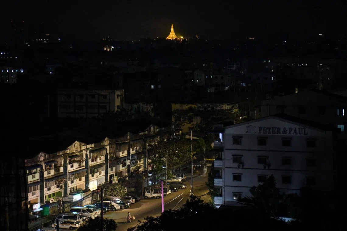 TOPSHOT - This photo taken on January 14, 2025 shows a man (down) riding his bike along a street, with the Shwedagon Pagoda seen in the background, during an electricity blackout in Yangon. (Photo by Sai Aung MAIN / AFP)