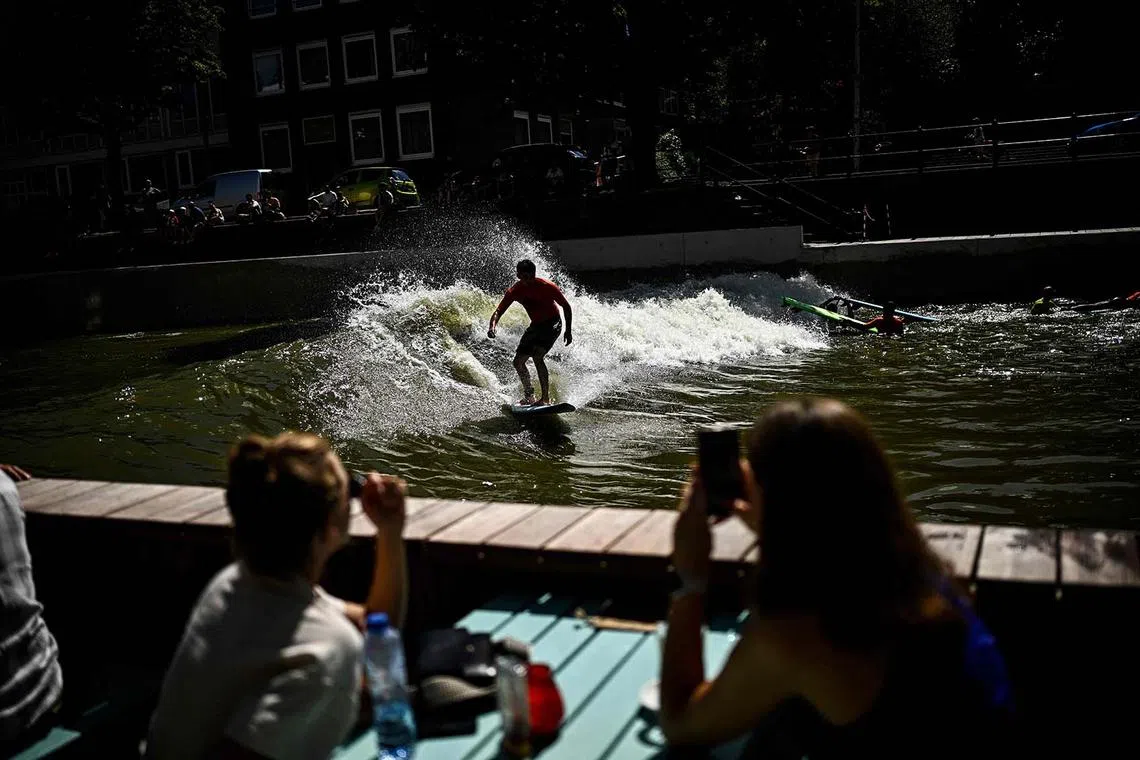 People watching a surfer riding on a canal while having a drink on a terrasse in Rotterdam on Aug 11, 2024.