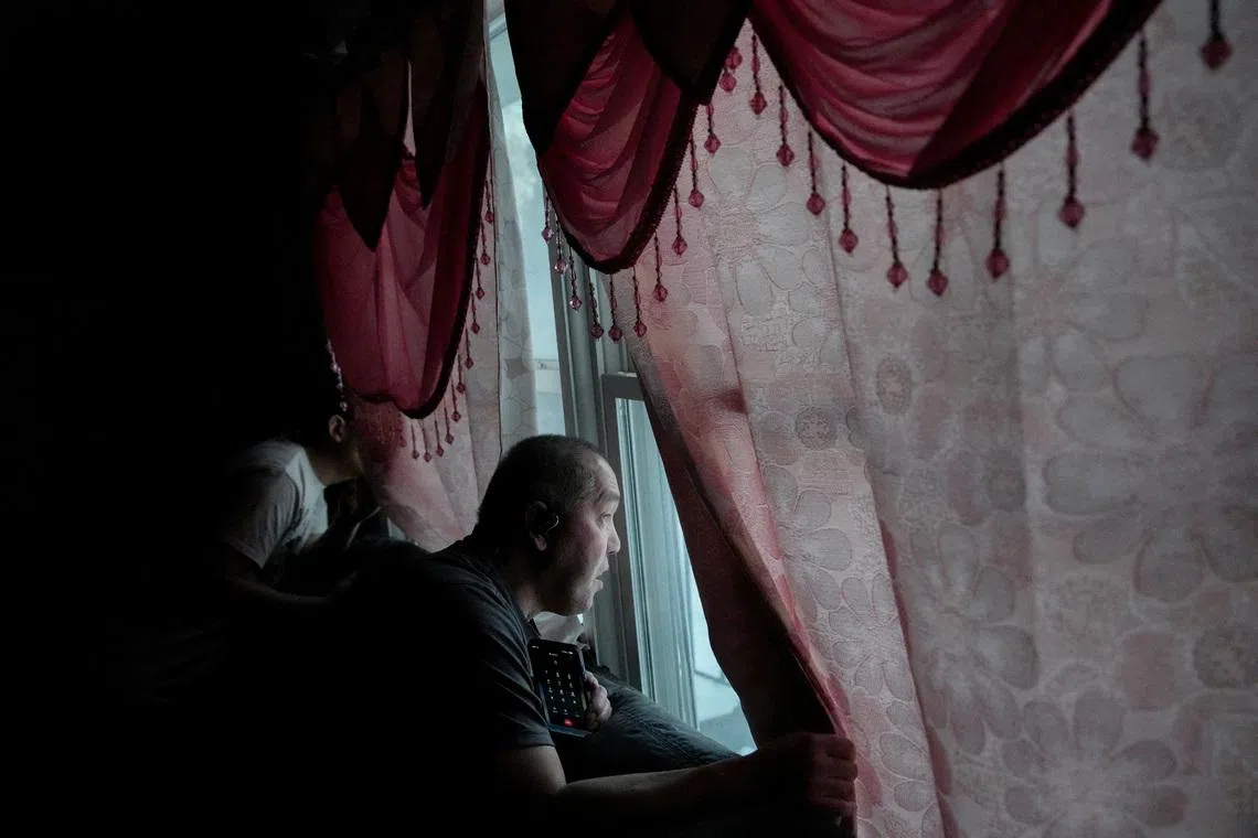 Scott Thao, looking out the window with his son Chris Thao as several vehicles with U.S. Immigration and Customs Enforcement (ICE) agents idle in the street outside of their home a day after he was taken by ICE agents and later returned in St Paul, Minnesota, U.S., Jan 19, 2026. He was eventually released as he's a U.S. citizen.