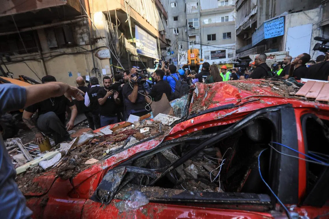 Bystanders and reporters check the destruction in a street after an Israeli strike in the Ghobeiri area of Beirut's southern suburbs.