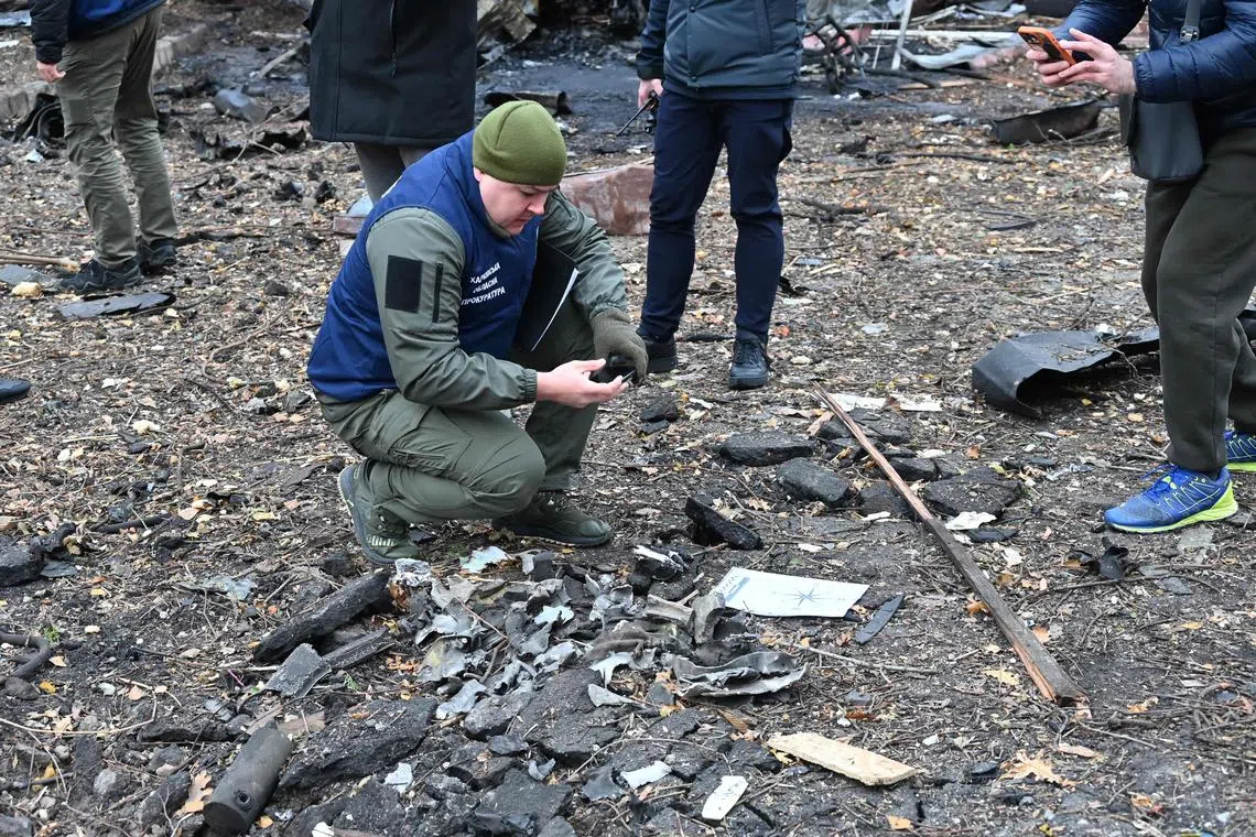 A Ukrainian war crimes prosecutor taking a photo on his mobile phone of the remains of a missile used during an attack in Kharkiv, in November 2024.