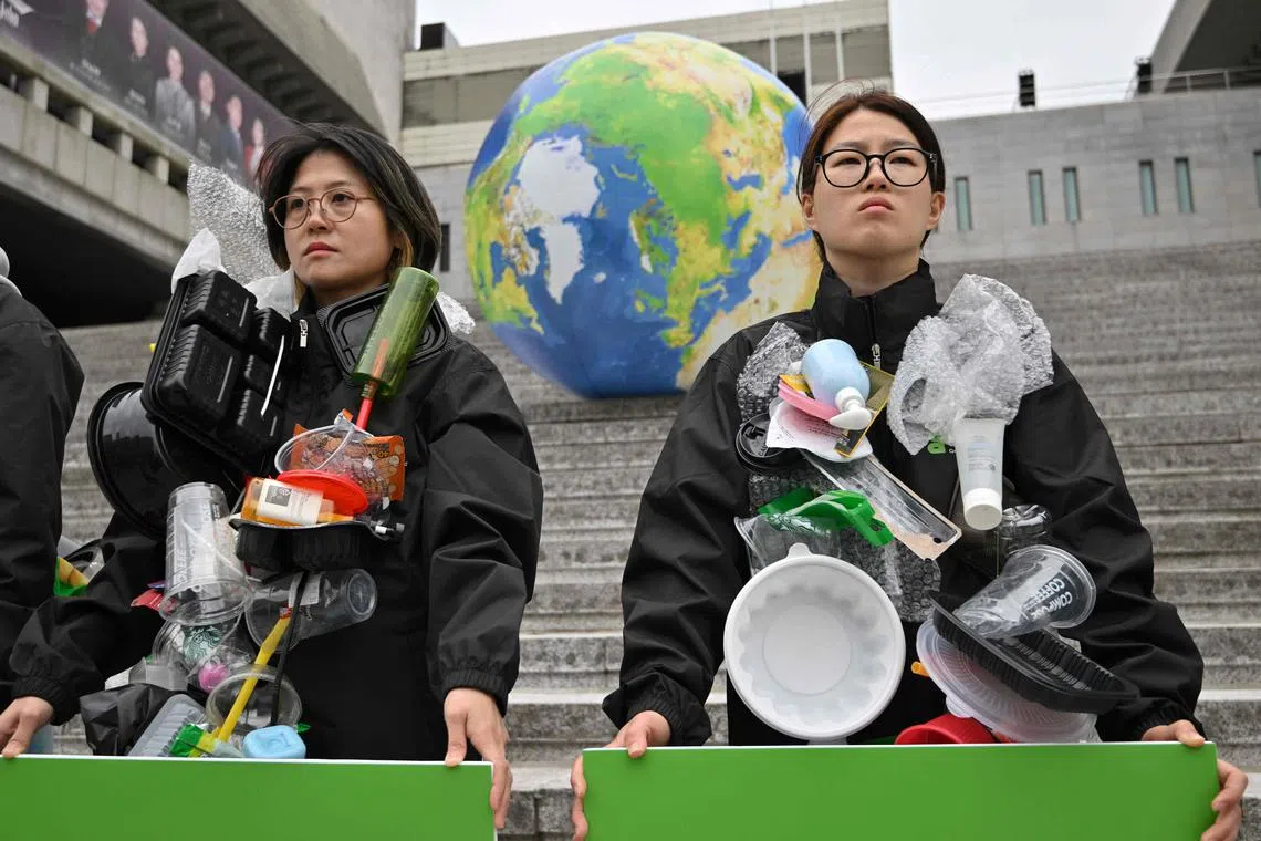 Activists decorated with plastic waste stand near an earth balloon during a campaign event to mark Earth Day in Seoul.