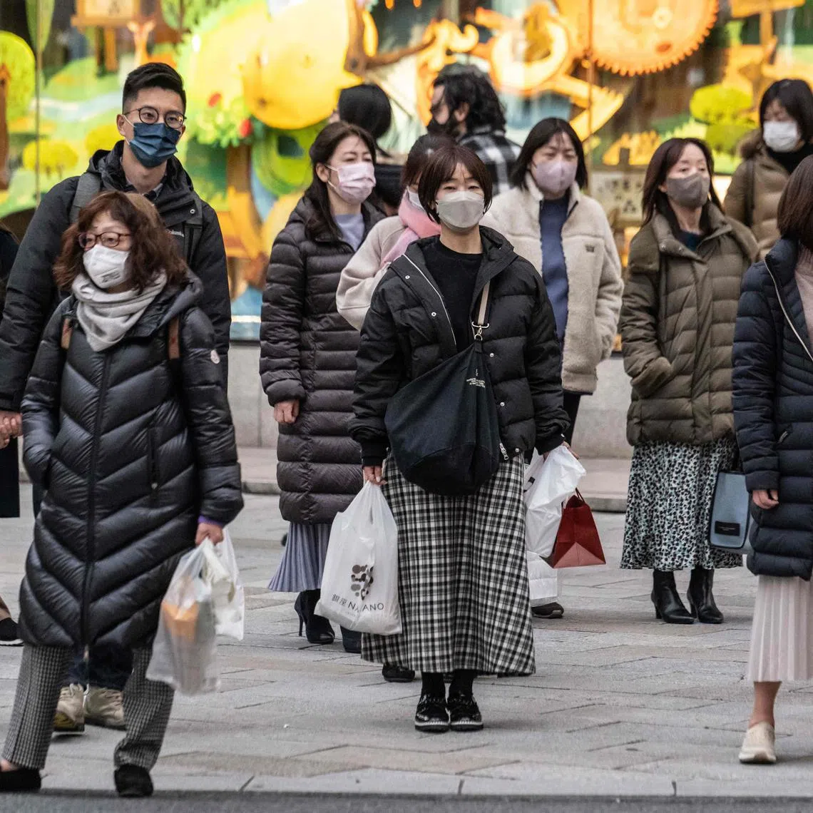 People wearing face masks wait to cross a street in Tokyo on Jan 27, 2023.
