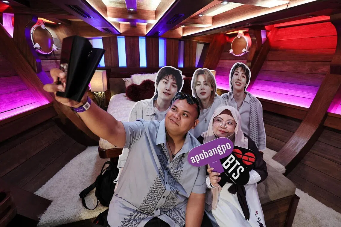 O oficial de apoio ao aprendizado Nurul Shafika (à direita), 32, e o segurança Talmizi Hamid (30) conversam em frente a um estande exibindo os membros do BTS (da esquerda) Suga, Jimin e J-Hope na cabine do proprietário do Royal Albatross.