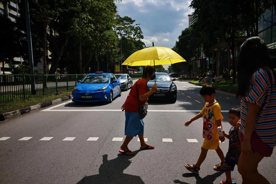 Elderly woman crossing the road using an umbrella to shade herself from the heat.