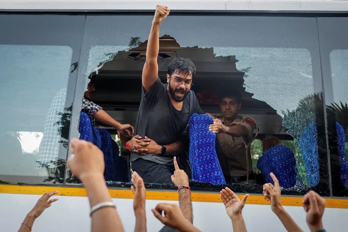 Police officers stop a demonstrator trying to jump out of a bus window broken by detained protesters in New Delhi, on Oct 4.