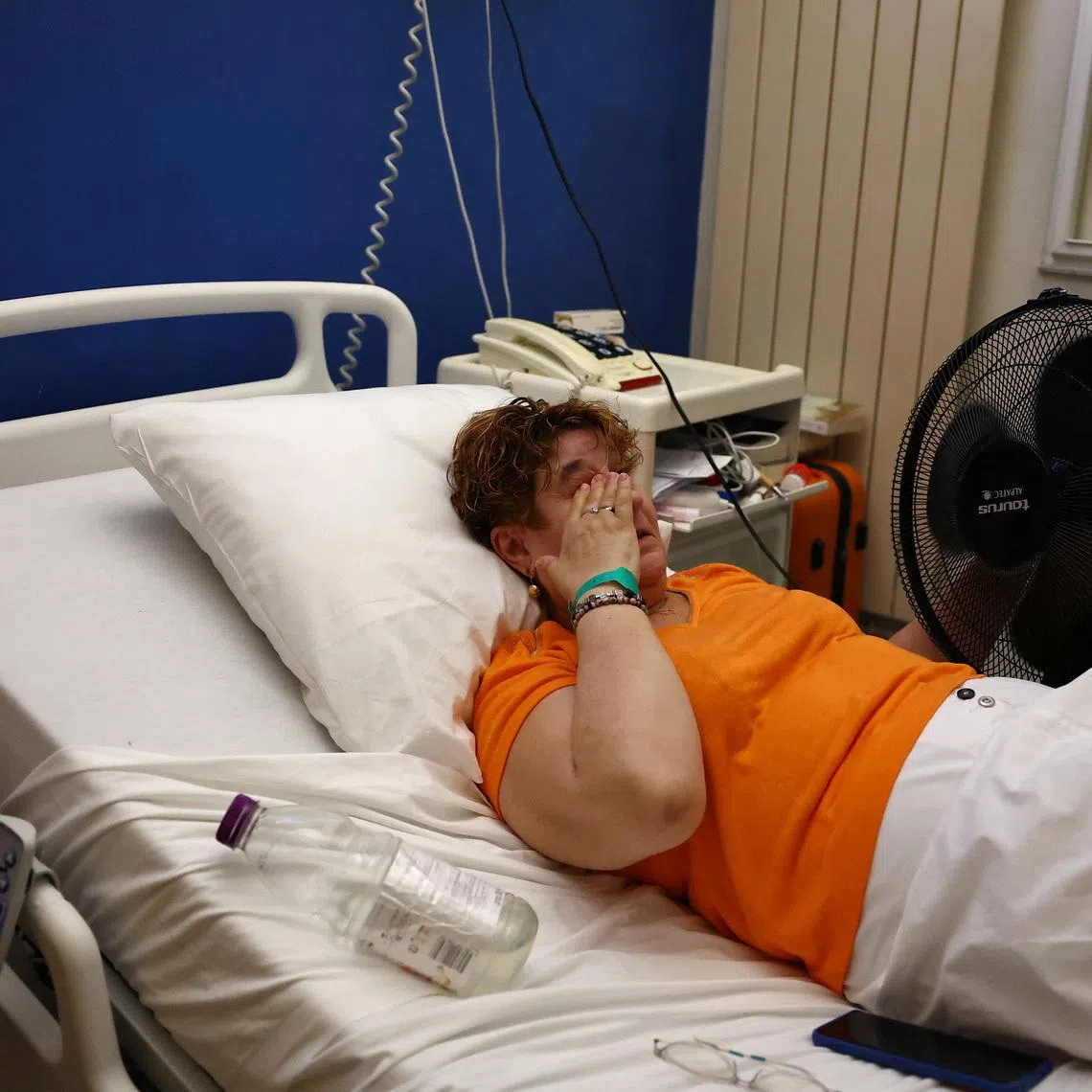 A patient lying in a hospital bed cools off with an electric fan at the Manhes Private Hospital in Fleury-Merogis near Paris during a heatwave affecting a majority of the country, France, June 25, 2026. REUTERS/Abdul Saboor