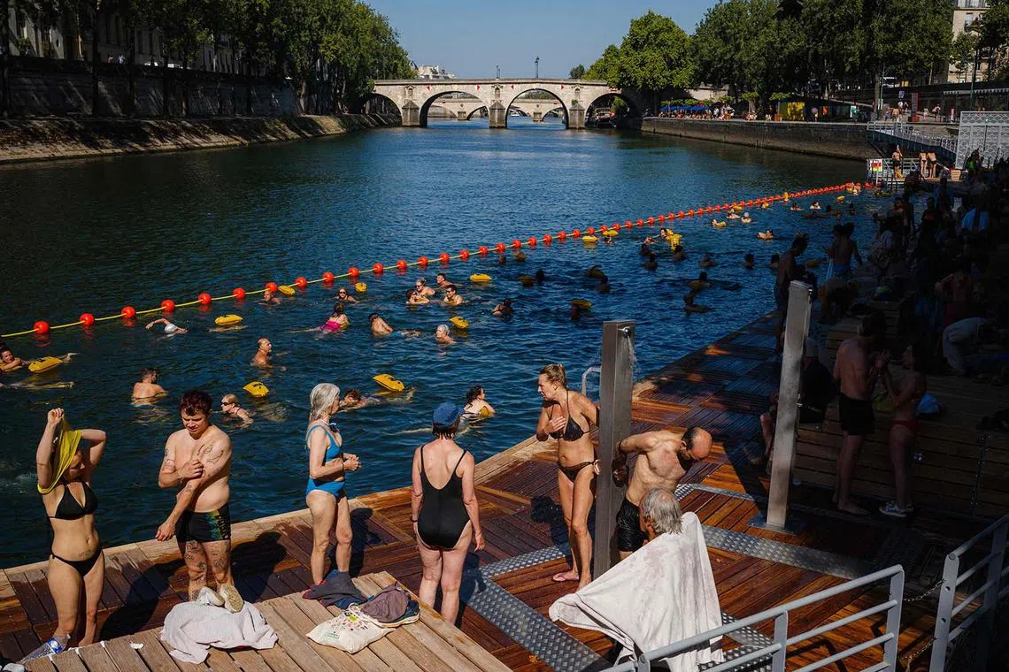 TOPSHOT - People swim and sunbath at the Bras Marie safe bathing site on the river Seine in Paris on August 12, 2025. France continues to suffocate with 14 departments in the southwest and southeast on red alert for heatwave on August 12, 2025, an exceptional heat wave, even for the month of August, which is prompting authorities to increase precautionary measures. (Photo by Dimitar DILKOFF / AFP)