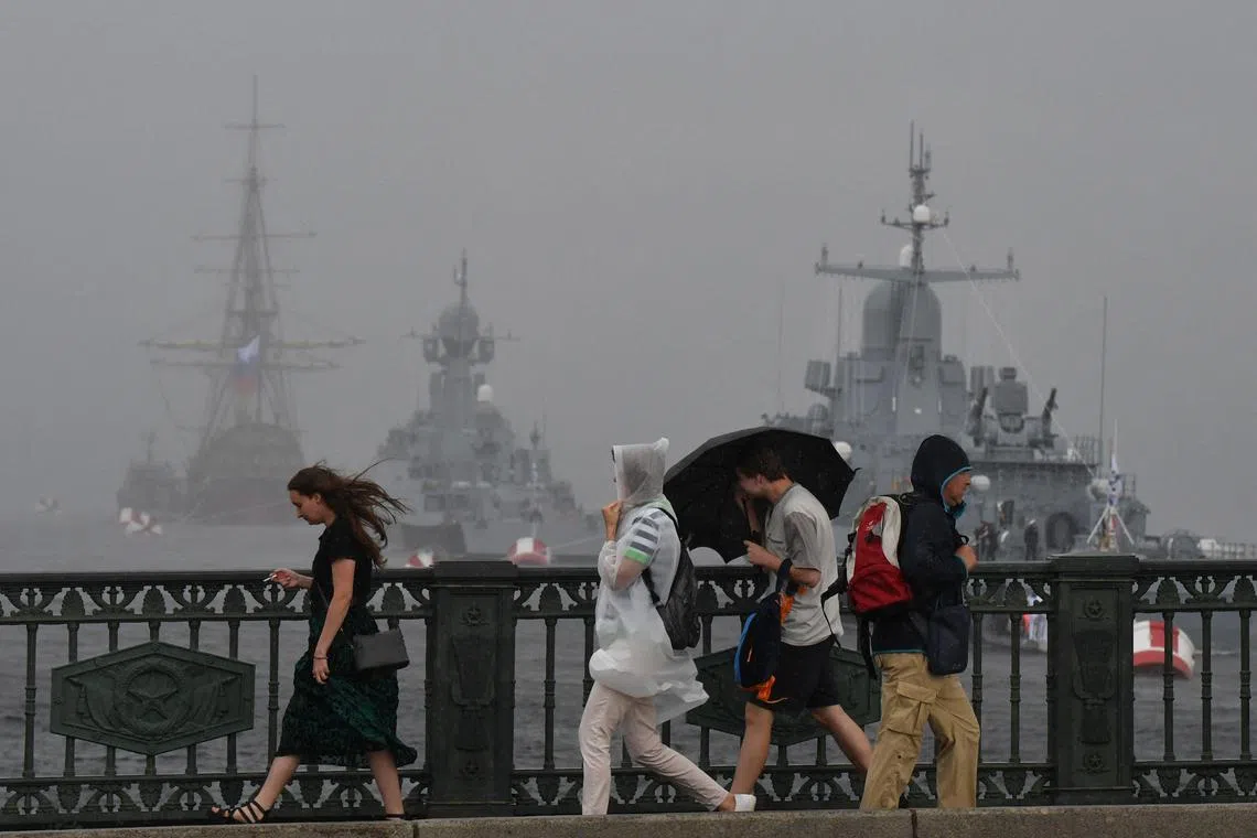 People cross the bridge as Russian small rocket ship 'Odintsovo' and small rocket ship of the 3rd rank 'Serpukhov' are seen on the Neva river during a rehearsal for the Naval parade in Saint Petersburg on July, 21, 2024. The celebration of Navy Day in Russia is traditionally held on the last Sunday of July and will be celebrated on July 28 this year. (Photo by Olga MALTSEVA / AFP)