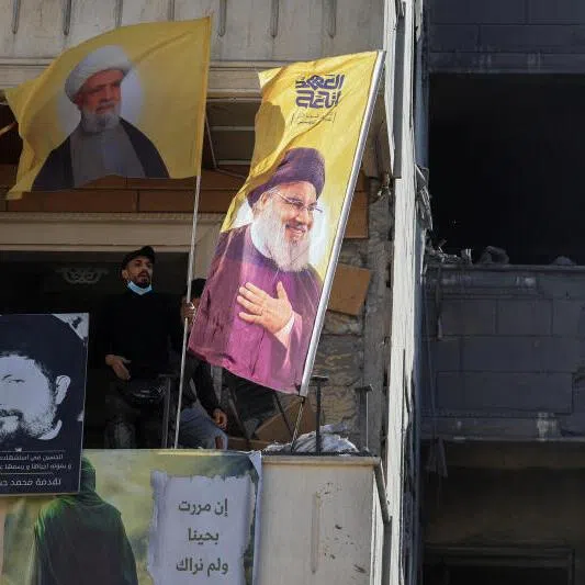 Hezbollah supporters looking out of a building damaged in an Israeli strike, with flags showing images of Hezbollah leaders Naim Qassem and Hassan Nasrallah at the site of an Israeli strike, in Choueifat, Lebanon, April 13, 2026.