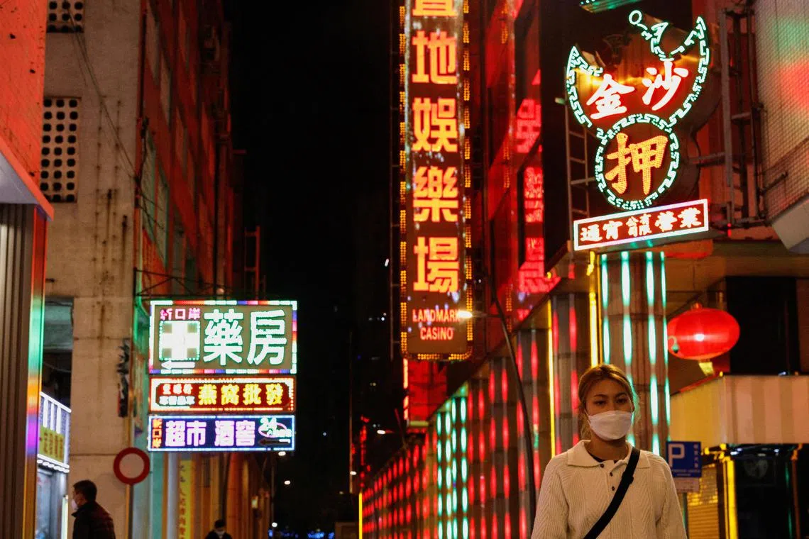 FILE PHOTO: A woman wearing face mask walks under neon lights near a casino during the coronavirus disease (COVID-19) pandemic in Macau, China, December 29, 2022. REUTERS/Tyrone Siu/File Photo