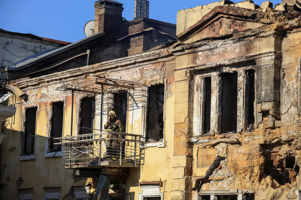 A person in protective gear stands on scaffolding attached to an old, multi-story building.
