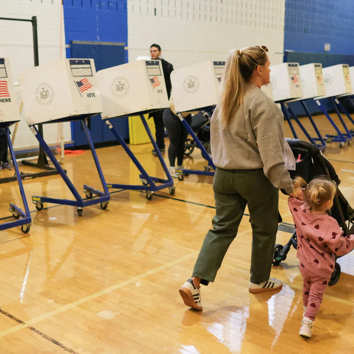 FILE PHOTO: A woman a her child walk past voting booths during the New York City mayoral election, at a polling site at the High School of Art and Design in the Manhattan borough of New York City, U.S., November 4, 2025. REUTERS/Brendan McDermid/File Photo