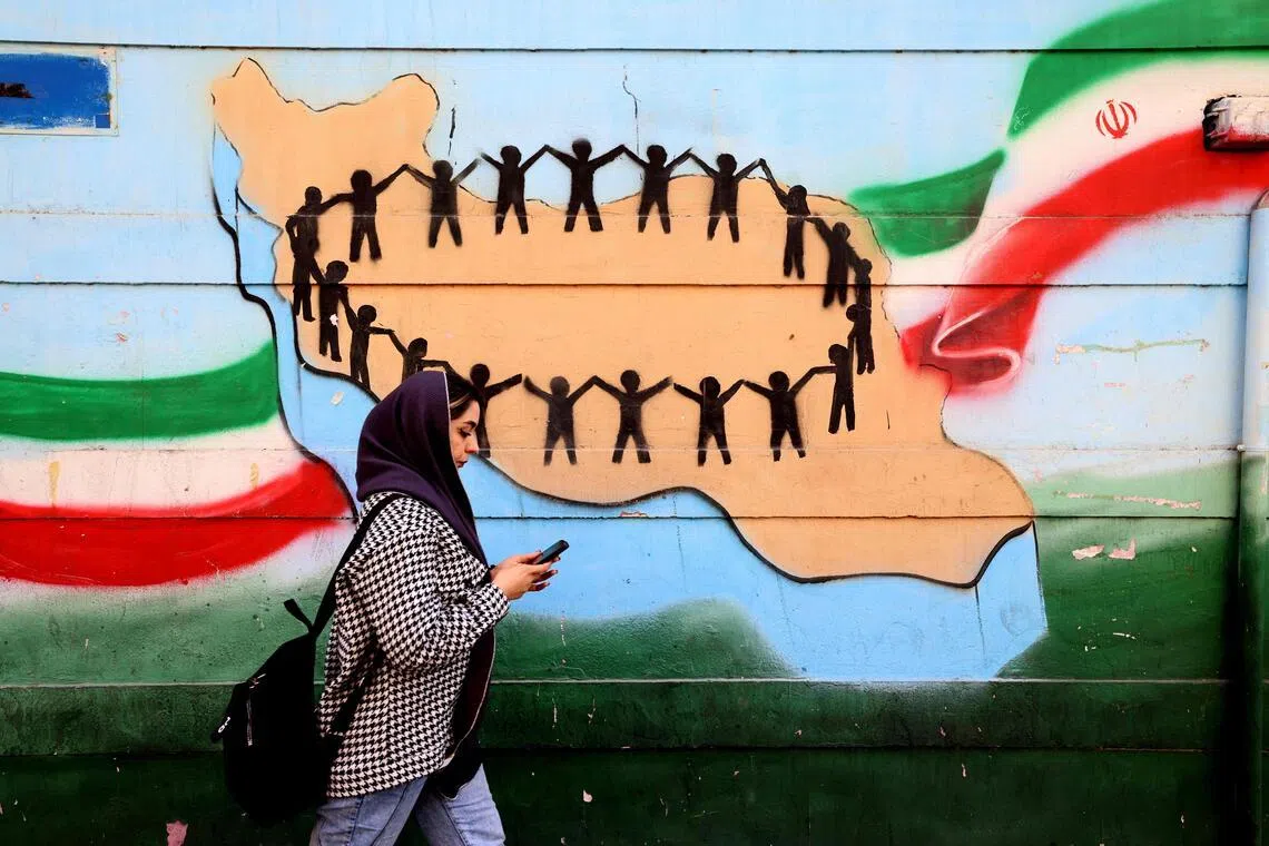 A woman walking past the flag and map of Iran painted on a wall in Tehran on Feb 25.