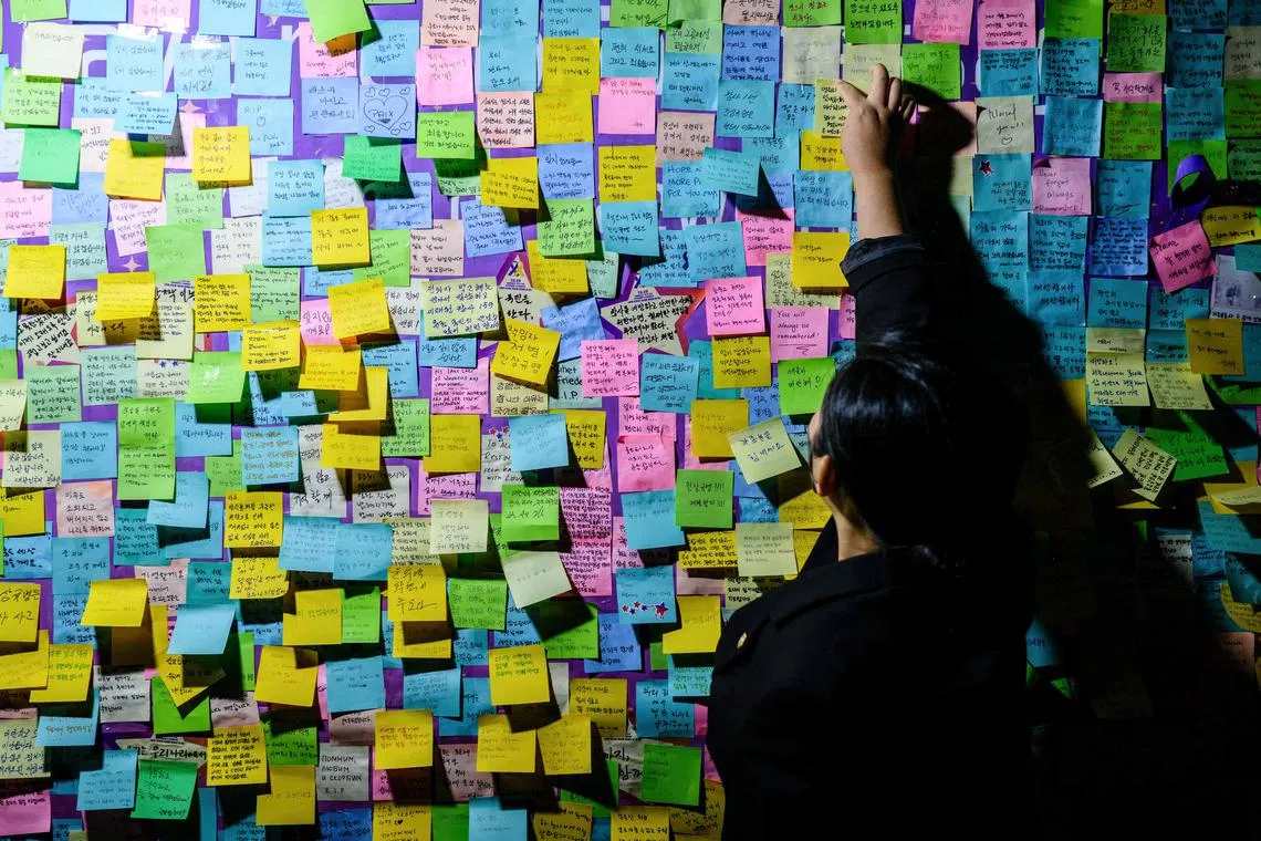 A person attaching a handwritten note next to others left on a board during a vigil in Seoul on October 29, 2023, to mark the first anniversary of the tragic crowd crush that killed 159 people during Halloween celebrations, in Seoul’s popular Itaewon nightlife area a year ago. 