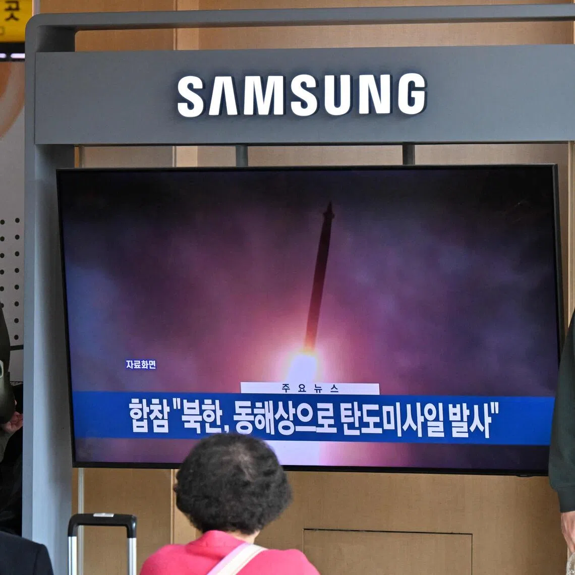 People stand next to a television showing a news broadcast with file footage of a North Korean missile test, at a railway station in Seoul on Nov 7, 2025. 