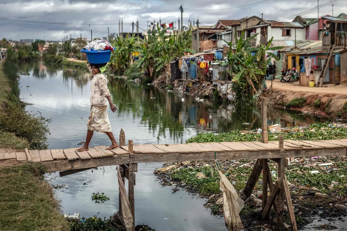 A woman carrying laundry as she crosses a bridge over a stream in Antananarivo, on Oct 5, 2025. 