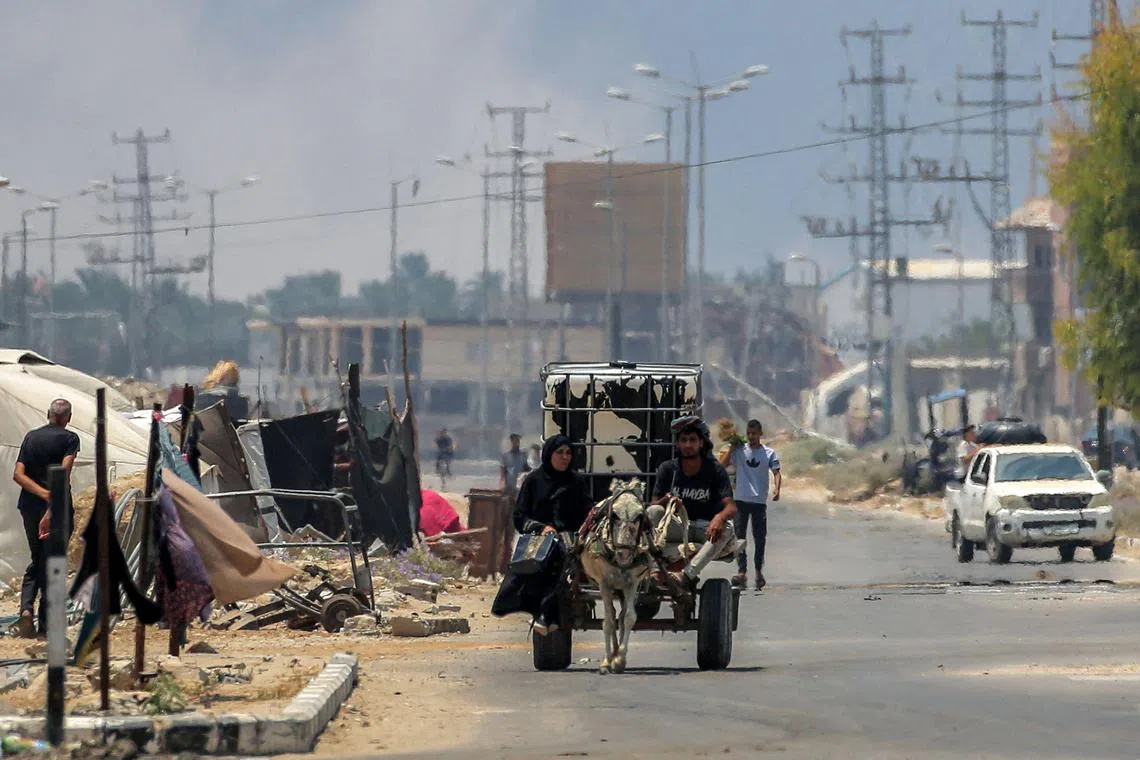 A man and woman riding in a donkey-drawn cart carrying a water cistern while smoke billows behind them from Israeli bombardment, in Deir el-Balah, in the central Gaza Strip, on July 21.