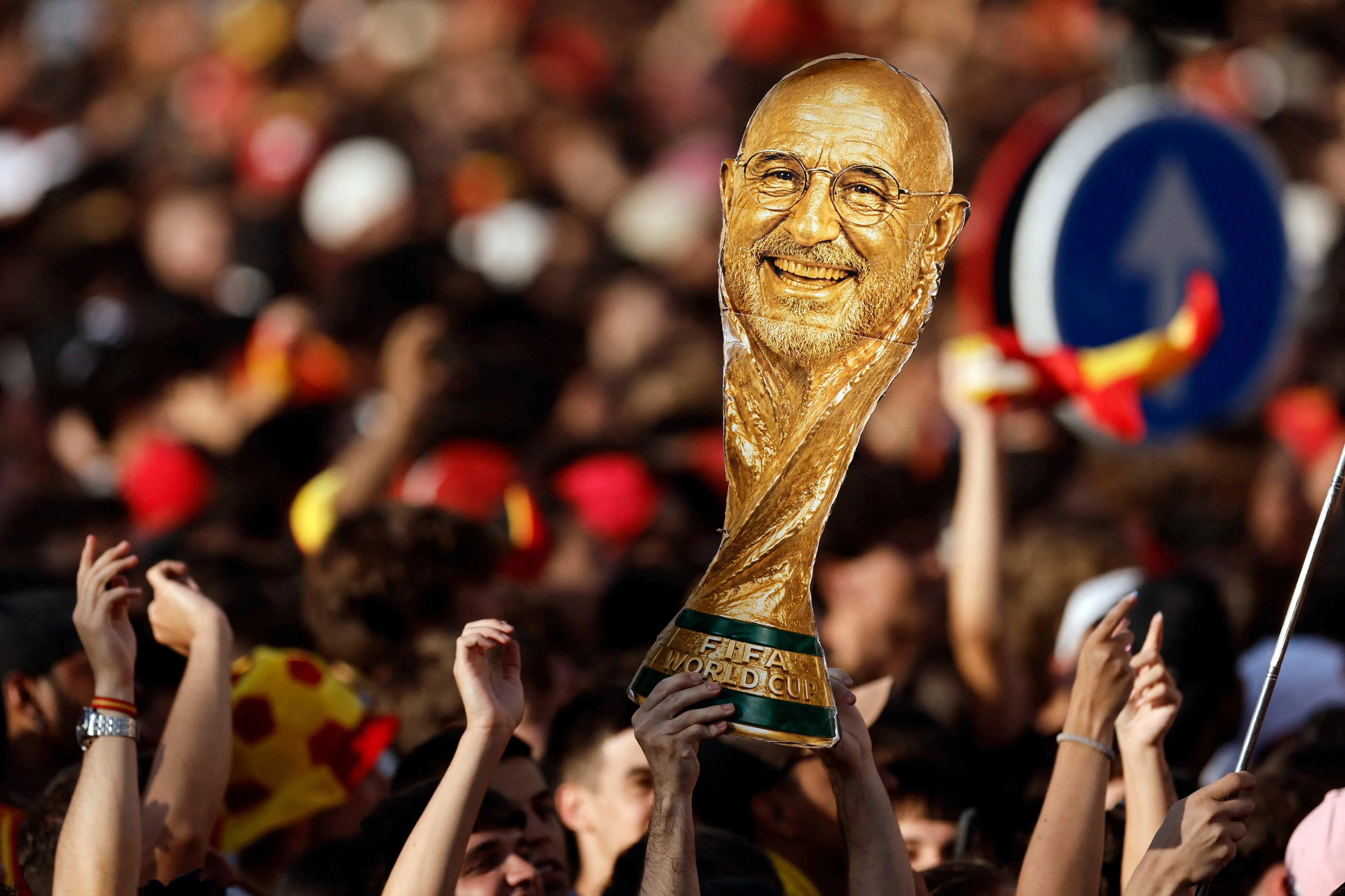 TOPSHOT - A person holds up a cardboard trophy cutout with Spain's coach Luis de la Fuente's face swapped onto it as Spain fans gather at Cibeles Square in Madrid on July 20, 2026, awaiting the arrival of the national football team one day after winning their second World Cup title following a 1-0 victory against Argentina. Spain's World Cup winners come back home to a heroes' welcome in Madrid, where a million fans are expected to greet them after a night of raucous celebrations across the country. (Photo by Oscar DEL POZO / AFP)