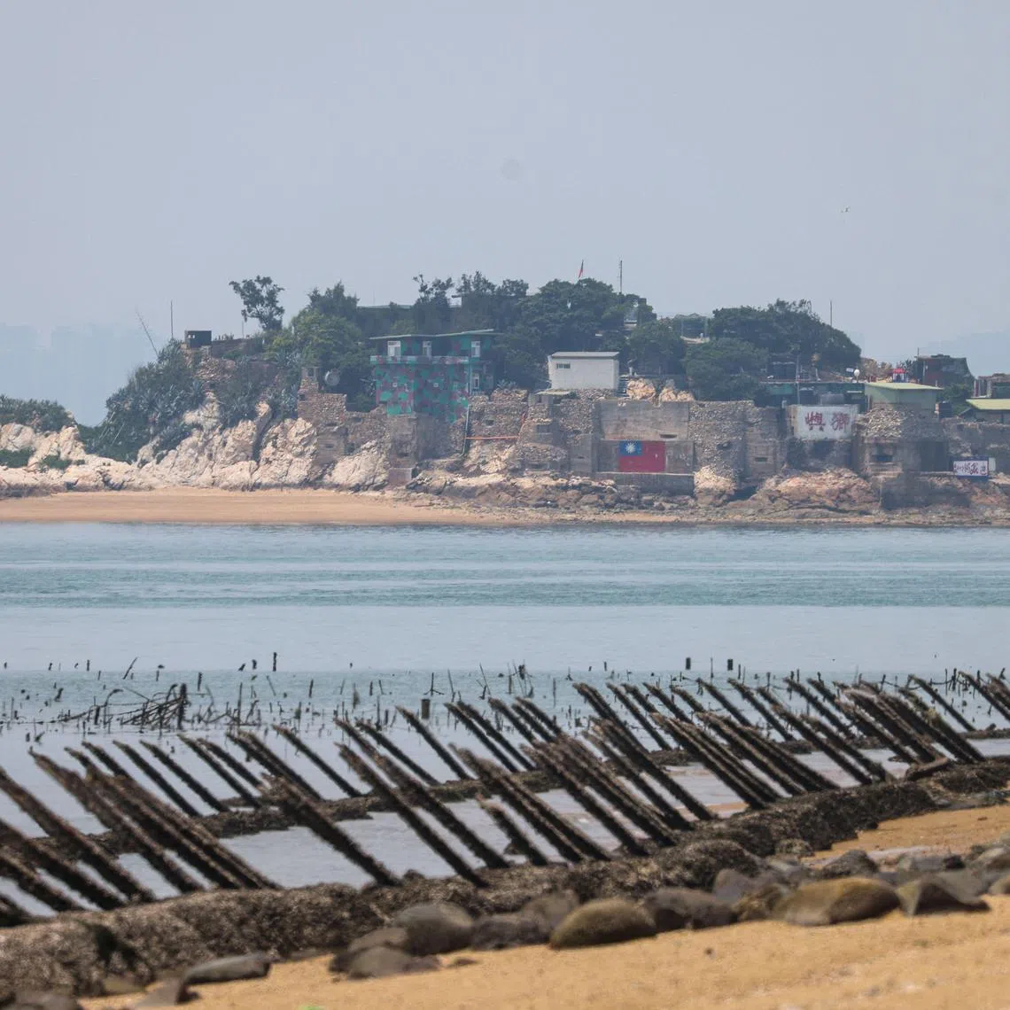A Taiwanese military outpost on Shihyu islet is seen past anti-landing spikes placed along the coast of Taiwan's Kinmen islands which lie just 3.2 kilometres (two miles) from the mainland China coast on May 18, 2024. Spikes jut from the beaches of Taiwan's Kinmen island, military checkpoints serve as traffic roundabouts and bunkers double up as tourist cafes -- reminders everywhere of the conflict decades earlier with Chinese communist forces. (Photo by I-Hwa CHENG / AFP)