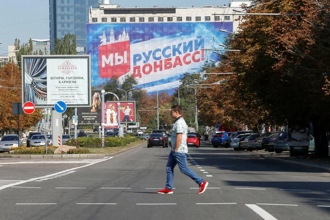 A pedestrian crosses a street near a building with a banner displaying the slogan \"We are Russian Donbass!\" in the rebel-held city of Donetsk, Ukraine September 9, 2021. REUTERS/Alexander Ermochenko/FIle Photo